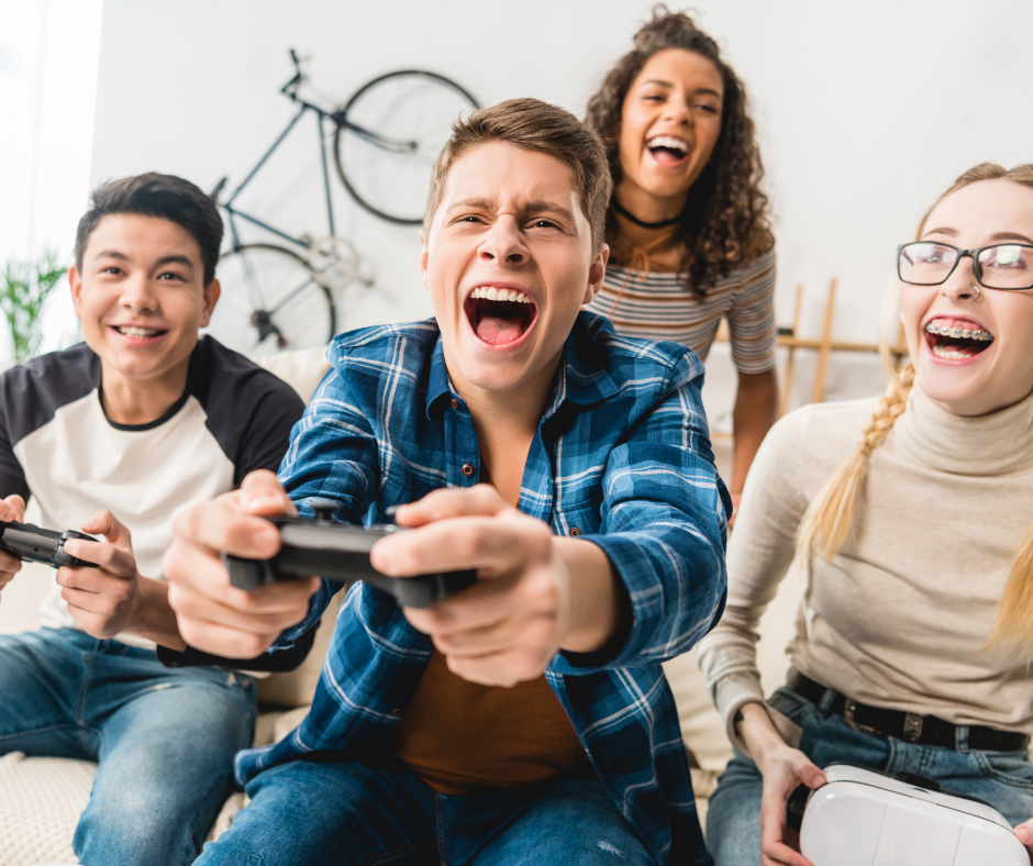Group of 4 teens playing video games and laughing. 