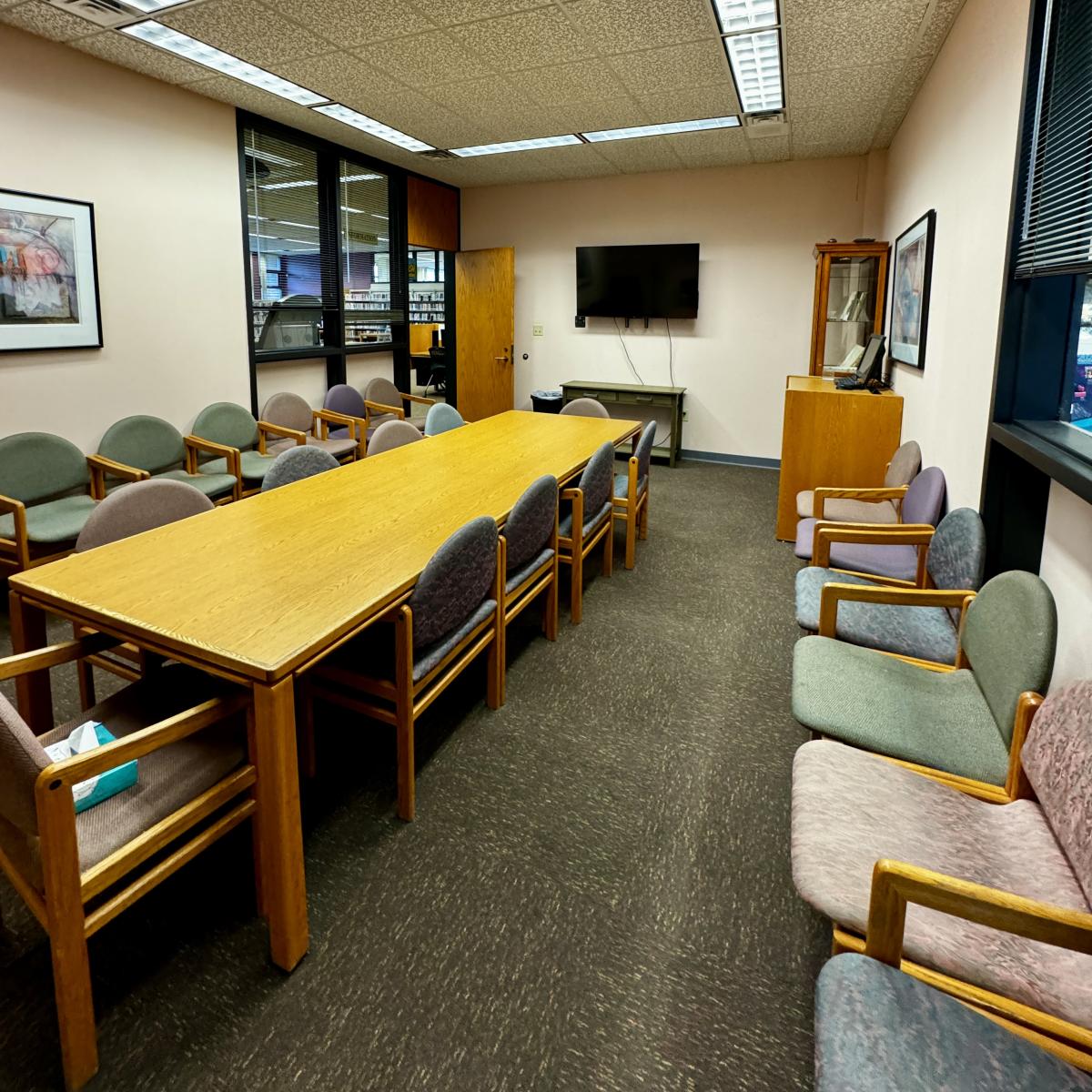 Long table with chairs, chairs along wall, TV on far wall, door on left.